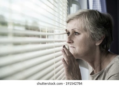 stock picture of scared elderly lady looking outside her window